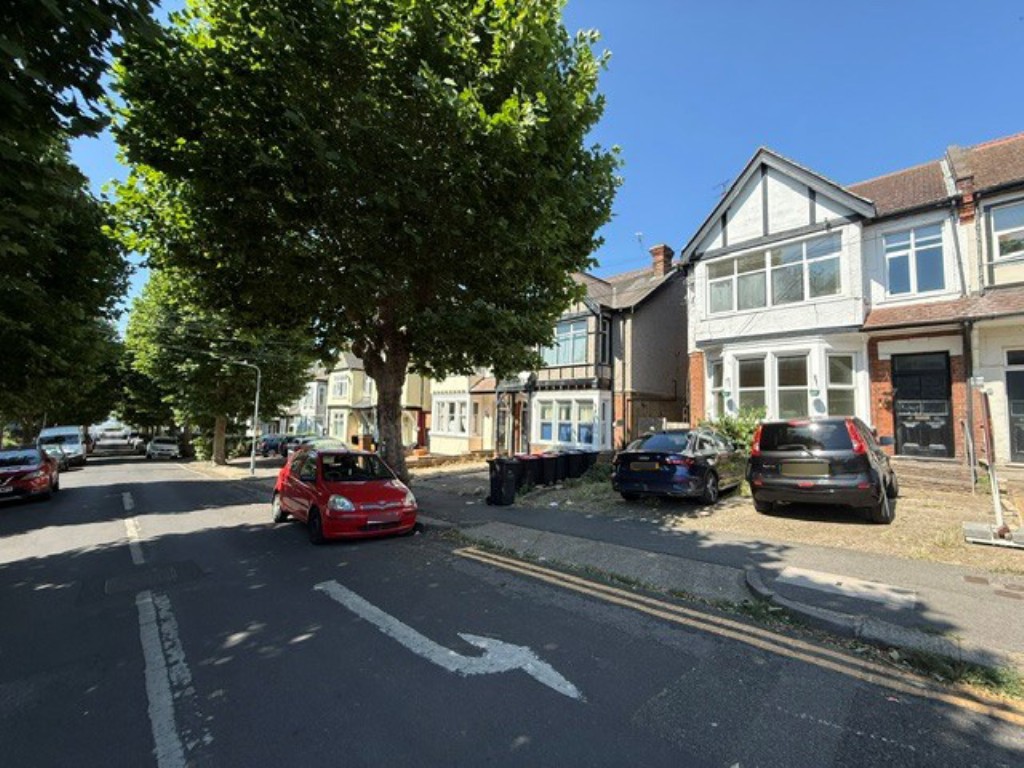 Lot: 180 - VACANT FIRST FLOOR FLAT FOR IMPROVEMENT - Street view with seafront at the bottom of tree lined road